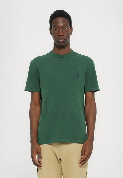 Groene katoenen t-shirt met een ronde hals en korte mouwen. Heeft een subtiele logo in een donkerder groen op de borst. Zachte textuur.