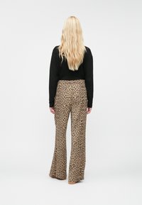 Lepardes druka platās kājas bikses ar gludu tekstūru, augstu jostasvietu un izplesti apakšējo malu; apvienotas ar melnu garām piedurknēm kreklu.