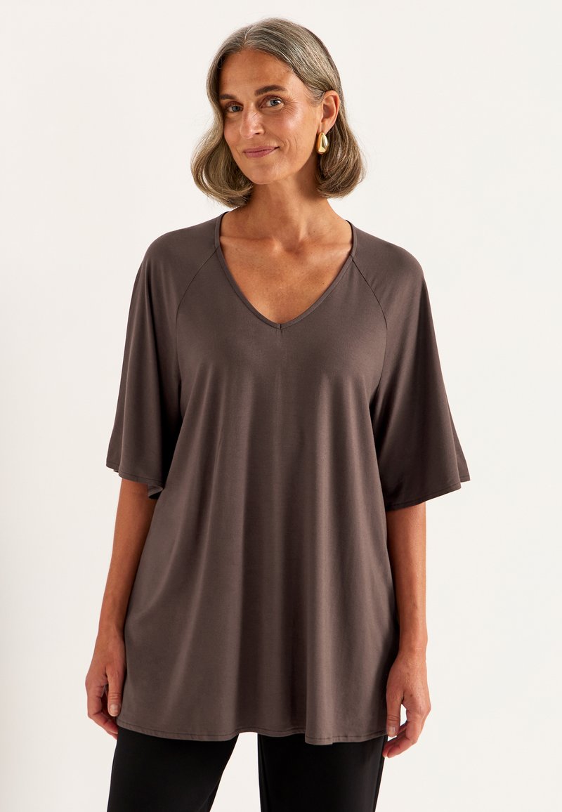 Bruine, lichte V-hals top met korte raglan mouwen, iets losse pasvorm, gladde textuur en casual stijl. Gekozen boven zwarte onderkleding.