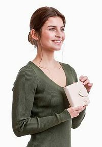 Čtvercová béžová kabelka s geometrickým zlatým akcentem, držena v rukou. Modelka má na sobě texturovaný olivově zelený žebrovaný svetr.