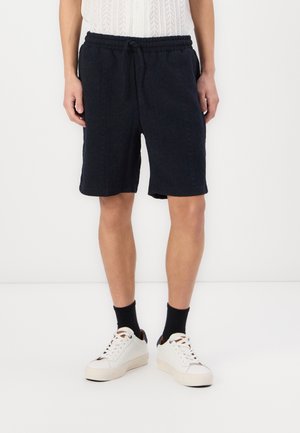 Navy blauwe shorts met een gestructureerd patroon, elastische tailleband en koordjes. Gecombineerd met witte sneakers en zwarte sokken.