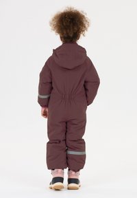 Bordeaux kleurig geïsoleerd sneeuwpak met capuchon, elastische taille en reflecterende accenten. Gecombineerd met zwarte en roze laarzen met een gestructureerd ontwerp.