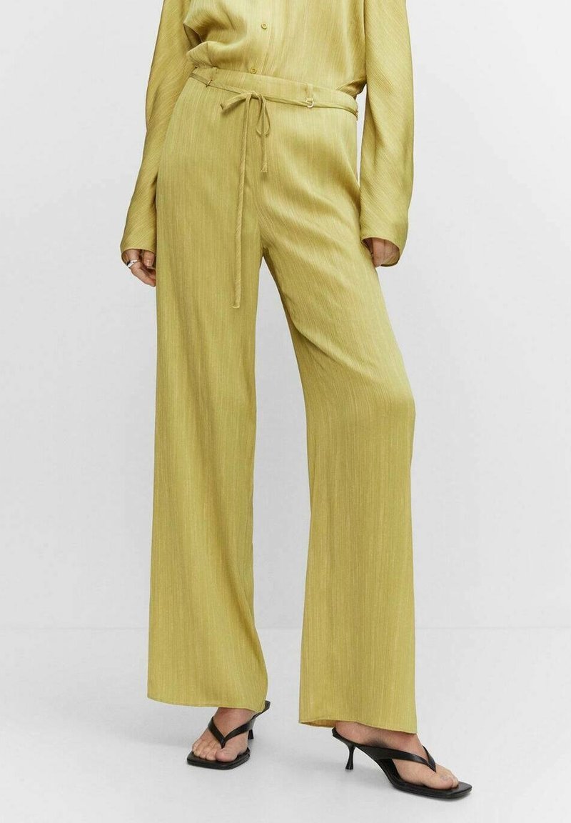 Pantalons larges en tissu texturé jaune clair avec une taille à cordon, associés à des sandales à talons noires.