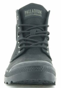 Botas de tobillo de lona negra con suela de goma, que presentan ojales de metal, cordones negros planos y un logotipo en la lengüeta. Detalles texturizados en la suela.
