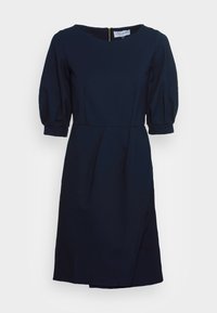 Mörkblå klänning med rundad halsringning, puffärmar och plisserad kjol. Utrustad med dragkedja i ryggen för stängning. Slät tygtextur.