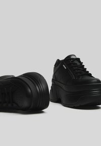 Svarta plattformssneakers med en texturerad läderovandel, vadderad krage och kontrasterande vita logotypdetaljer. Har tjocka gummisulor.