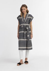 Abito avvolgente a maniche corte, con motivo blu navy e crema, dotato di una cintura, abbinato a pantaloni bianchi e sandali neri testurizzati.