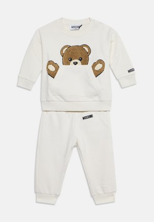 Ensemble sweat-shirt et pantalon bébé couleur crème avec un motif ours en peluche à l’avant et le logo Moschino sur la manche et la ceinture.