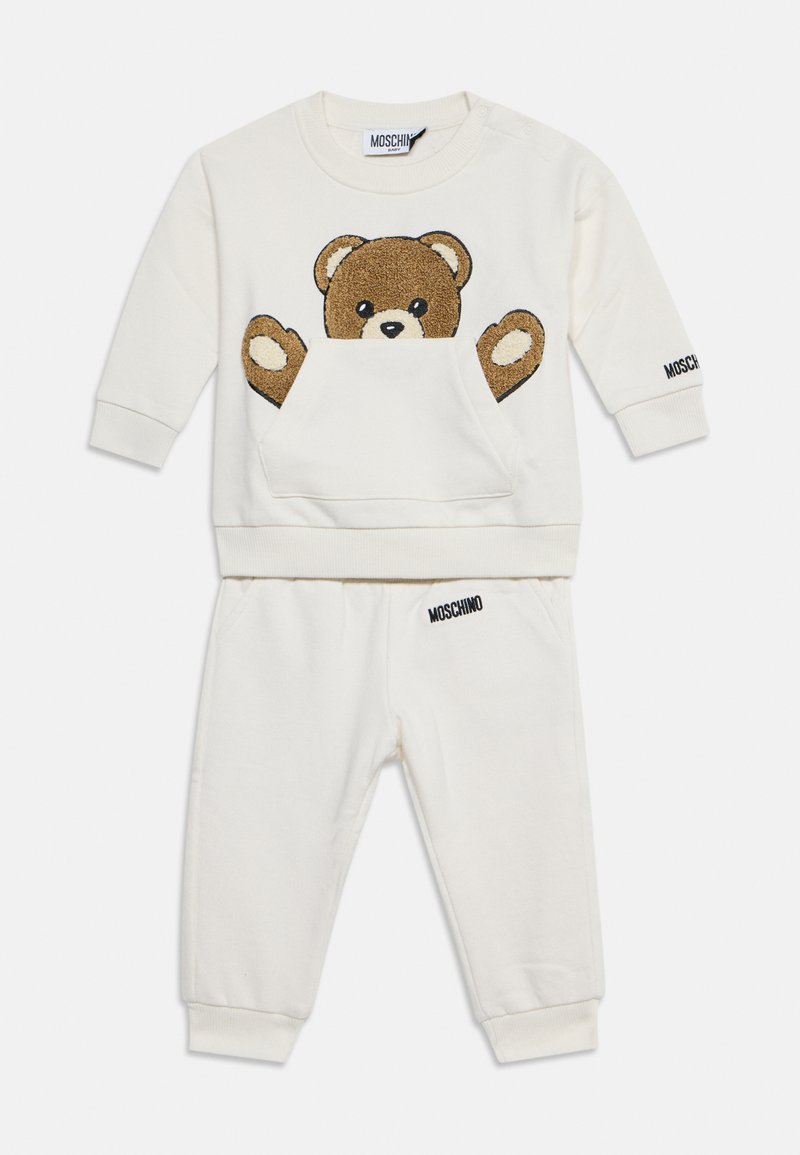 Ensemble sweat-shirt et pantalon bébé couleur crème avec un motif ours en peluche à l’avant et le logo Moschino sur la manche et la ceinture.