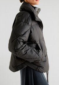 Sort puffer-jakke med høj krave, quiltet tekstur og sidelommer. Har et strømlinet design og elastisk kant for en tætsiddende pasform.