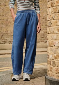 Pantaloni ușori, albaștri, cu șnur la talie, au o croială lejeră, buzunare laterale și detalii cusute. Asortați cu adidași albi.