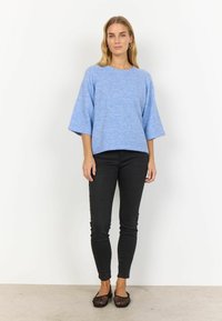 Hellblauer Strickpullover mit weit geschnittenen Ärmeln, kombiniert mit schwarzen, eng anliegenden Jeans und schwarzen Netz-Ballerinas. Einfaches Design, weicher Stoff.