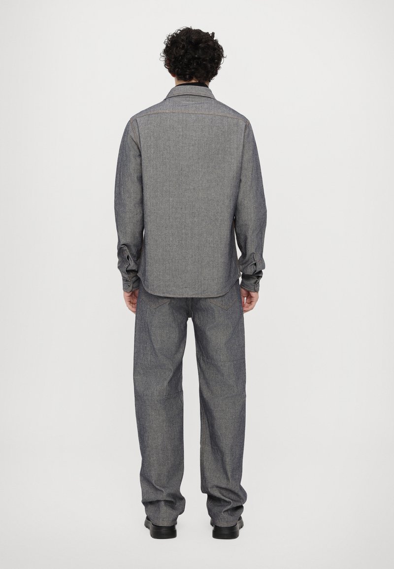 Grå denimskjorta och byxor, lös passform, med långa ärmar och krage med knappar. Påfallande sömdetaljer och texturerad tyg.