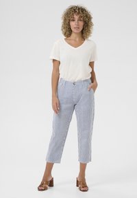 Cream V-neck T-shirt paired with blue and white striped cropped trousers. The trousers feature a buttoned waistband and side pockets.
