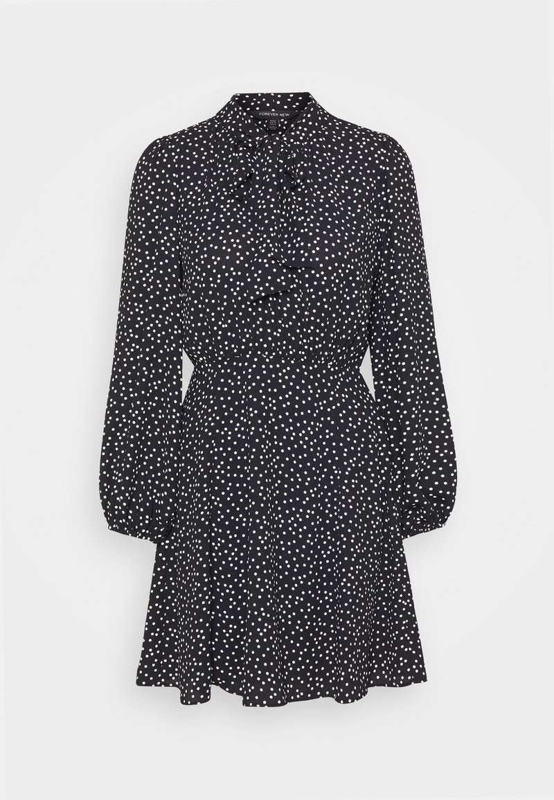 Robe noire à pois blancs, manches longues bouffantes, taille froncée et nœud noué au col.