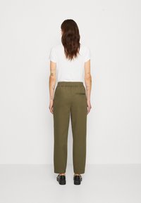 Olijfgroene, loszittende broeken met een elastische tailleband, zij- en achterzakken, en een gladde textuur. Draag een wit t-shirt erbij.
