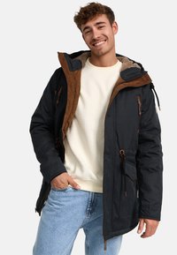 Mørkeblå parka-jakke med brune suede-detaljer, struktureret shearling-fore, justerbar drawstring talje og lynlåslommer foran.