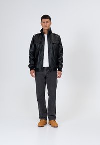 Czarna skórzana kurtka typu bomber z dwoma frontowymi kieszeniami, ściągaczami na mankietach i stójką. W zestawie z szarymi dżinsami i brązowym obuwiem.