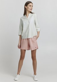 Lys grøn linned skjorte med trekvartærmer og henley-neckline, kombineret med lyserøde linned shorts og hvide sneakers.