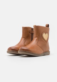 Bottines en cuir marron avec une fermeture éclair sur le côté, bout rond et un patch en forme de cœur beige avec des détails de couture sur le côté extérieur.