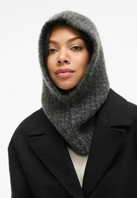 Bufanda con capucha de punto gris oscuro, hecha de un material suave y texturado, llevada sobre un abrigo negro. La bufanda tiene un ajuste ceñido alrededor del cuello.