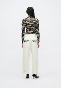 Διαφανές τοπ με μακριά μανίκια σε μαύρες και μπεζ ζέβρες ρίγες, συνδυασμένο με ψηλόμεσο λευκό παντελόνι που διαθέτει ριγέ τσέπες στο πίσω μέρος. Μαύρα τακούνια.