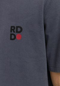 Pilkas medvilninis marškinėlis su juodu "RD" ir "DO" teksto logotipu bei raudonu taškeliu, trumpomis rankovėmis ir laisvu, priglitusiu dizainu.