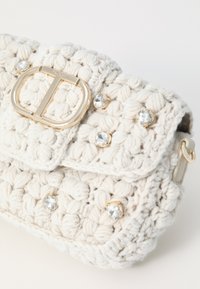 White crocheted bag with gold hardware and crystal accents, featuring a textured surface and a flap closure with a rectangular buckle.