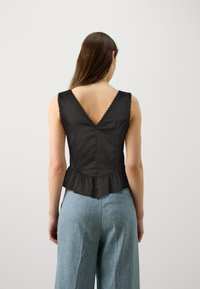 Sort satin peplum top med V-rygdesign og blondekant på ærmerne samt en struktureret pasform. Kombineret med lys blå brede bukser.