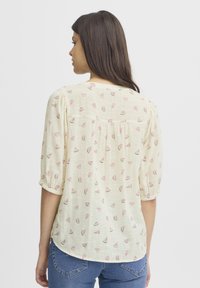 Lichtbeige blouse van lichtgewicht stof met een achterpaneel en korte pofmouwen. Bevat herhaalde roze watermeloenpuntpatronen.