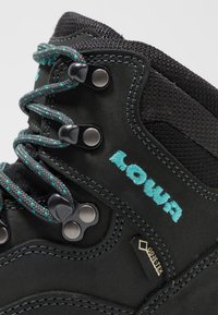 Zwarte wandelschoen met turkooise veters en logo. Beschikt over metalen veteroogjes, een getextureerde bovenkant en een Gore-Tex label aan de zijkant.