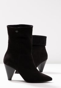 Bottines en daim noir avec un talon conique effilé, dotées d'un revers plié et de détails de coutures subtiles. Texture lisse et bout pointu.
