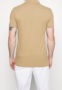 Beige poloko s límečkem a krátkými rukávy, vyrobené z hladké tkaniny. Má jemnou texturu a volný střih.