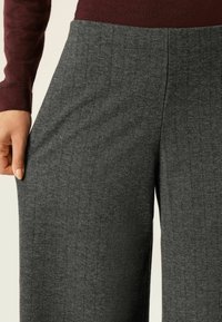 Szare spodnie w szerokim kroju w wzór houndstooth, wykonane z fakturowanej tkaniny, z gładką talią i ręką opartą na boku, prezentując materiał.