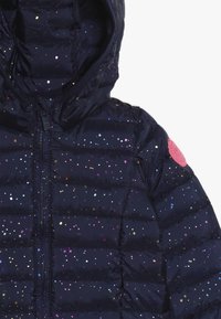 Marineblå pufferjakke med en blank finish, der har multikolorede paljetter, hætte og lyserød logo-lap på ærmet. Quiltet design, lynlåslukning.