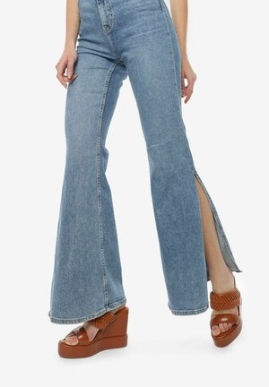 Lichtblauwe flared jeans met zijslitsen, gemaakt van denim. Gecombineerd met bruine wedge sandalen met een geweven banddetail.