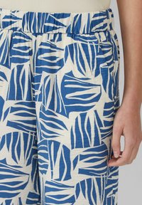 Blauwe en witte broek met een bladerenpatroon, voorzien van een elastische tailleband en zakken. De stof lijkt zacht en ademend.