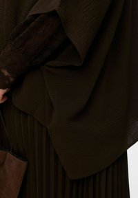 Tenue marron superposée comprenant un haut texturé à manches larges et une jupe plissée. Des accents en dentelle foncée sur les manches rehaussent le design.