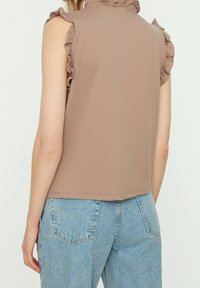 Brun ærmeløs top med bølgede skulderdetaljer; glat tekstur og en afslappet pasform, parret med lyseblå denimjeans.
