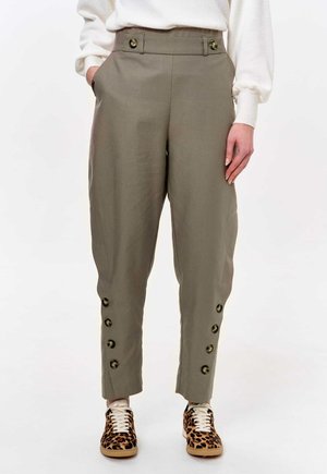 Khaki tailored trousers with front pockets, button accents on cuffs, and a medium-rise fit, paired with animal-print sneakers.