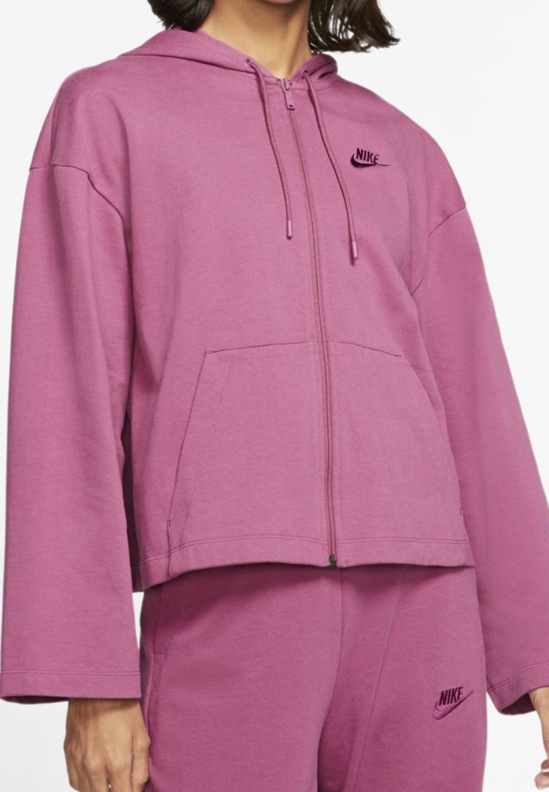 Roze fleece hoodie met een rits, voorzakken, capuchon met trekkoord en geborduurd Nike-logo op de borst. Losvallend ontwerp.