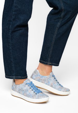 Light blue textured sneakers with thick white soles and matching blue laces worn with dark blue denim jeans on a white background.