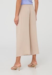 Pantaloni beige a gamba larga realizzati in tessuto leggero e morbido, con vita elasticizzata e un design fluido. Indossati con sandali con tacco di colore chiaro.