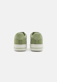 Zöld textúrájú sportcipők fehér talppal, perforált dizájnnal és dombornyomott márkázással a saroknál. Alacsony szárú stílus, lekerekített orral.
