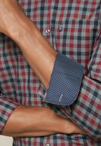 Rood en marineblauw geruit overhemd met contrasterende marineblauwe stippen op de manchetten en een klein borstzakje. Katoenen materiaal, slim fit.