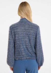 Flauschige, weiche blaue Strickjacke mit einem strukturierten Strickdesign, langärmelig und mit einem runden Kragen, von hinten betrachtet.