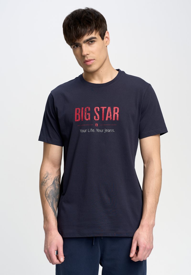 Camiseta de algodón azul marino con un diseño impreso en rojo que dice "BIG STAR" y "Tu Vida. Tus Jeans.". Cuello redondo clásico y mangas cortas.