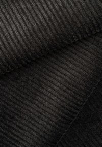 Dunkel geripptes Gewebe mit einer weichen Textur. Die Farbe weist unterschiedliche Schattierungen von Schwarz und Anthrazit auf und betont das geschichtete Erscheinungsbild.
