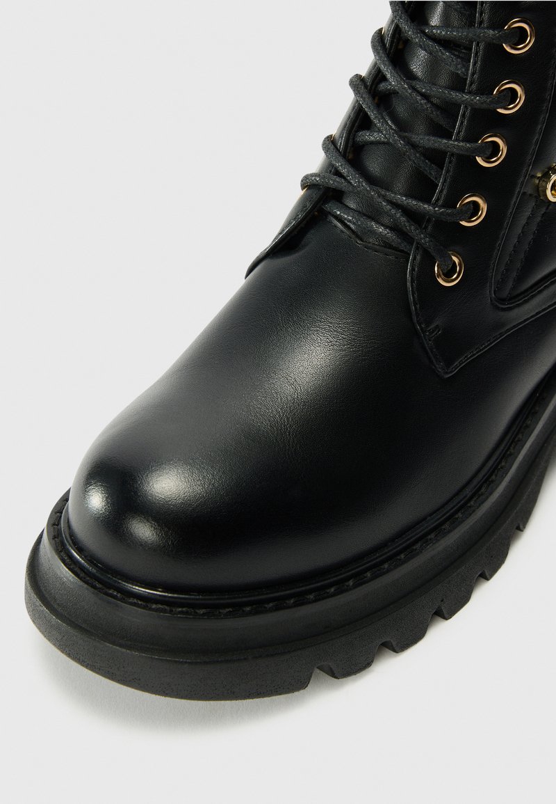 Zwarte leren enkelboot met een ronde neus, textuur op de bovenzijde, gouden oogjes voor de veters en een chunky, gestructureerde zool.