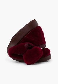 Bordeaux fluwelen pantoffels met een zachte, ronde vorm, voorzien van een prominente strik en een bruine rubberen zool voor grip en duurzaamheid.